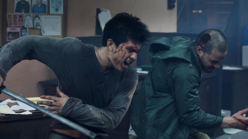 A still from Headshot shows Iku Uwais holding a machete charging as a man behind him bleeds from the head