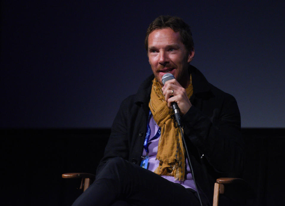 Benedict holds a microphone while speaking on stage