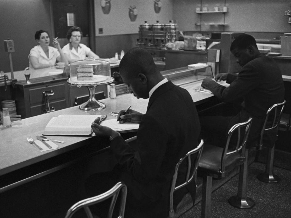 African American students from Saint Augustine College study while participating in a sit-in at a lunch counter reserved for white customers in Raleigh, North Carolina. Two waitresses look on from the other side of the counter.
