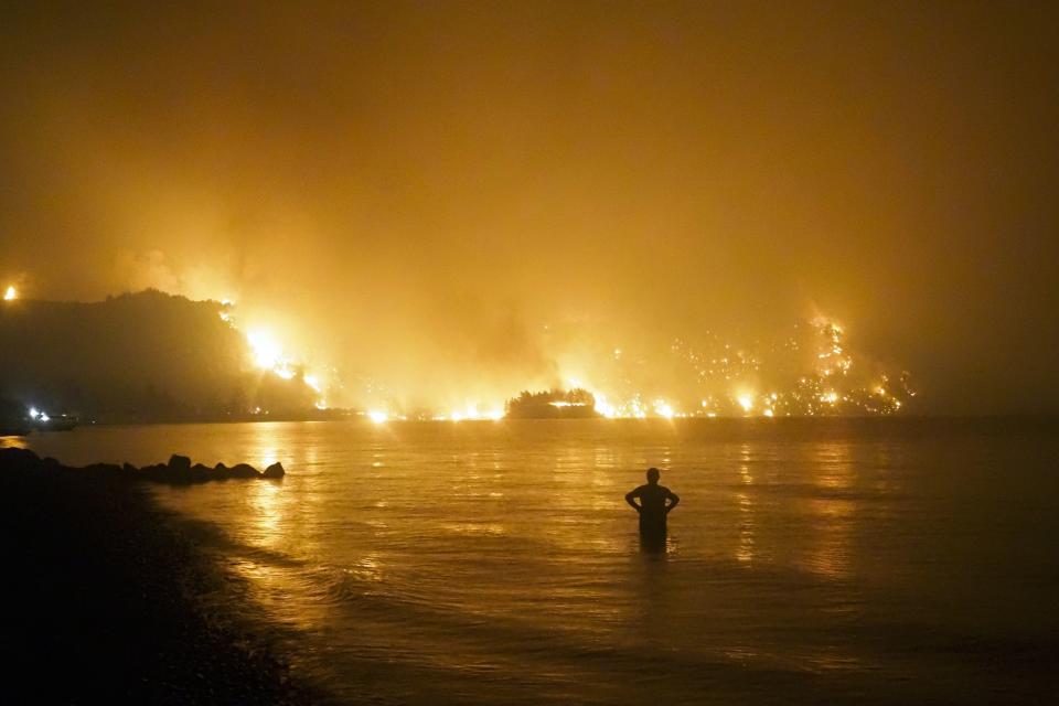 FILE - A man watches as a wildfire approaches Kochyli beach near the village of Limni, on the Evia island, Greece, about 160 kilometers (100 miles) north of Athens, on Aug. 6, 2021. In Greece, which suffered some of Europe's most devastating fires last August, authorities say higher fuel costs have added to challenges facing the Fire Service that relies heavily on water-dropping planes to battle blazes in the mountainous country. (AP Photo/Thodoris Nikolaou, File)