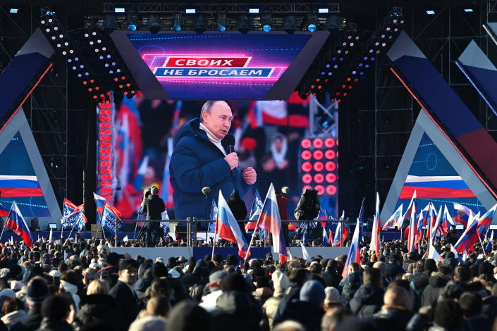 An audience holding flags watches a broadcast of Russian President Vladimir Putin's speech.