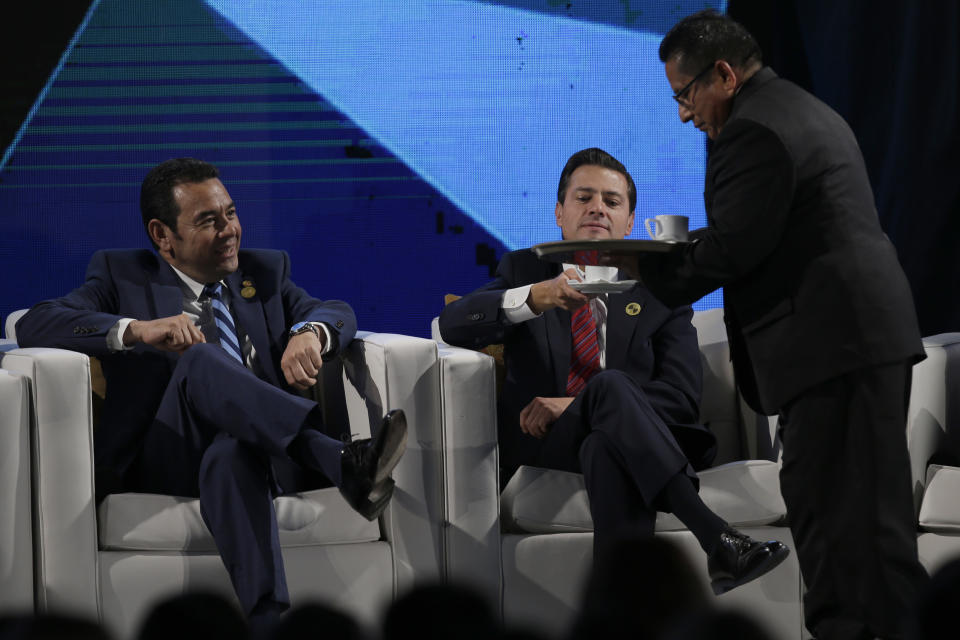 Mexico's President Enrique Pena Nieto, center, receives a cup of coffee as he sits next to Guatemala's President Jimmy Morales during an economic forum as part the XXVI Iberoamerican Summit in Antigua, Guatemala, Thursday, Nov. 15, 2018. The event is a biennial two-day meeting of heads of state from Latin America and the Iberian Peninsula. (AP Photo/Moises Castillo)