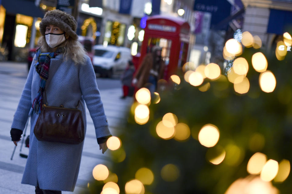 A woman wears a face mask as she walks past a Christmas tree in New Bond Street, in London, Tuesday, Dec. 22, 2020. Britain's Prime Minister Boris Johnson cancelled Christmas for almost 18 million people across London and eastern and south-east England, following warnings from scientists of the rapid spread of the new variant of coronavirus.(AP Photo/Alberto Pezzali)