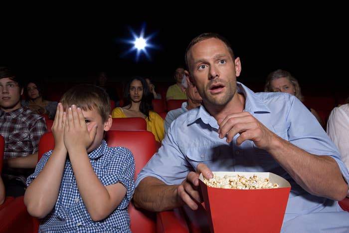 kid covering his eyes while dad eats popcorn