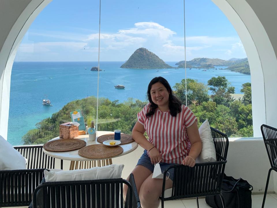 A woman posing for a picture at a table with a window overlooking tropical water and islands.