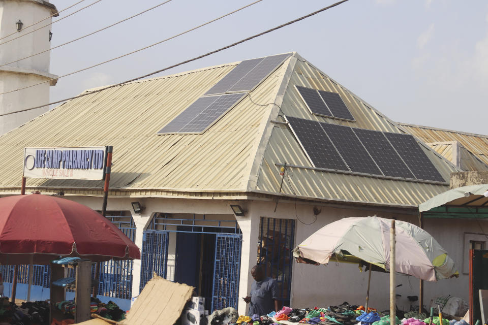 A man sells shoes outside a shop with solar panels on the roof in Abuja, Nigeria, Saturday June 17, 2023. Nigeria's removal of a subsidy that helped reduce the price of gasoline has increased costs for people already struggling with high inflation. But it also potentially accelerates progress toward reducing emissions in Africa's largest economy. (AP Photo/Olamikan Gbemiga)