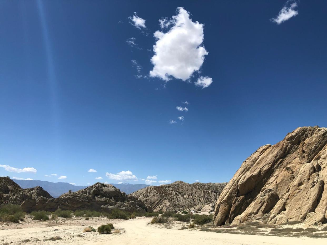 Clouds float above the sandy washes and leaning rock formations