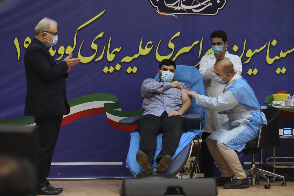 Parsa Namaki, center, son of Health Minister Saeed Namaki, receives a Russian Sputnik V coronavirus vaccine as Minister Namaki applauds, in a staged event at Imam Khomeini Hospital in Tehran, Iran, Tuesday, Feb. 9, 2021. Iran on Tuesday launched a coronavirus inoculation campaign among healthcare professionals with recently delivered Russian Sputnik V vaccines as the country struggles to stem the worst outbreak of the pandemic in the Middle East with its death toll nearing 59,000. (AP Photo/Vahid Salemi)