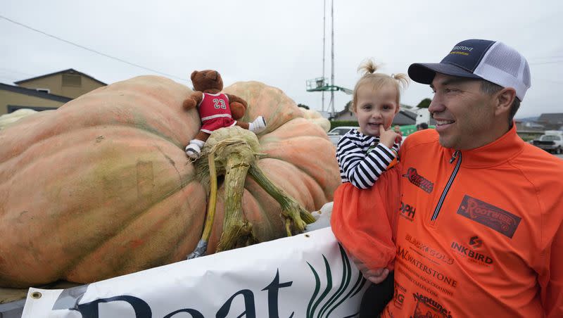 Travis Gienger of Anoka, Minn., holds his two-year-old daughter Lily while looking at his pumpkin called “Michael Jordan” before it was weighed at the Safeway 50th World Championship Pumpkin Weigh-Off in Half Moon Bay, Calif., Monday, Oct. 9, 2023. A pumpkin grown by Gienger won the event in 2022.