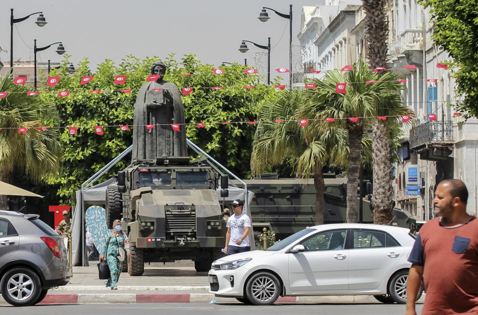 Tunisians walk past a military armored personnel carrier at Habib Bourguiba avenue in Tunis, Tunisia, Friday, July 30, 2021. Days of political turmoil in Tunisia over the economy and the coronavirus have left its allies in the Middle East, Europe and the United States watching to see if the fragile democracy will survive. (AP Photo/Hassene Dridi)