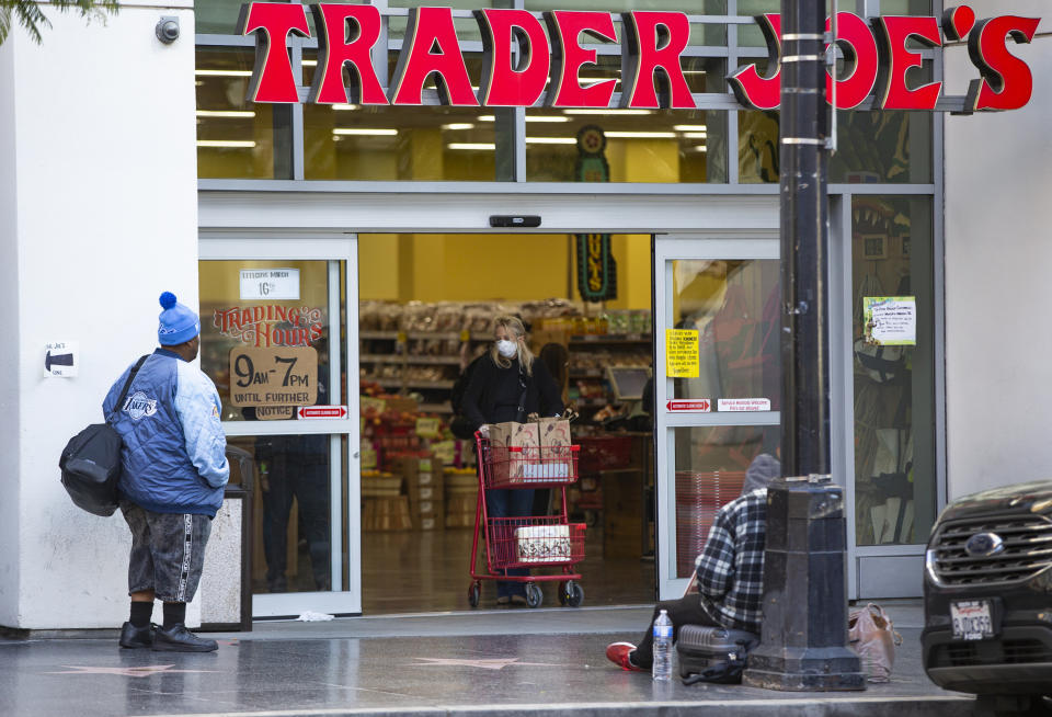 FILE - A person waits to enter a Trader Joe's grocery store, as a shopper leaves in the Hollywood section of Los Angeles on March 24, 2020. Millions of workers whose jobs don’t provide paid sick days are having to choose between their health and their paycheck as the omicron variant of COVID-19 rages across the nation. While many companies instituted more robust sick leave policies at the beginning of the pandemic, those have since been scaled back with the rollout of the vaccines, even though the omicron variant has managed to evade them. (AP Photo/Damian Dovarganes, File)