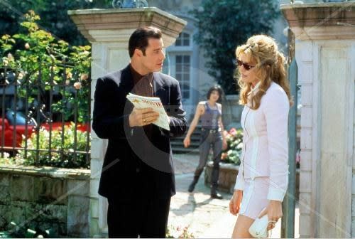 John Travolta and Rene Russo stand in a garden