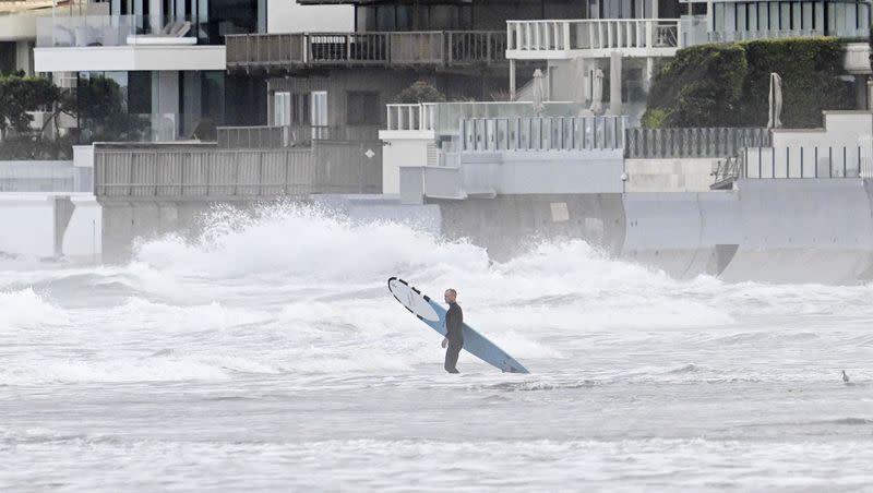 A surfer enters the water at La Jolla Shores Tuesday, Jan. 23, 2024, in La Jolla, California. Millions of California residents are currently under flood watches.