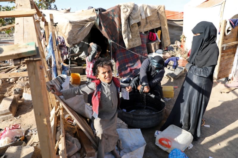 Samirah Nasser washes clothes as her daughter and sons stand outside a hut where they live at a camp for internally displaced people near Sanaa