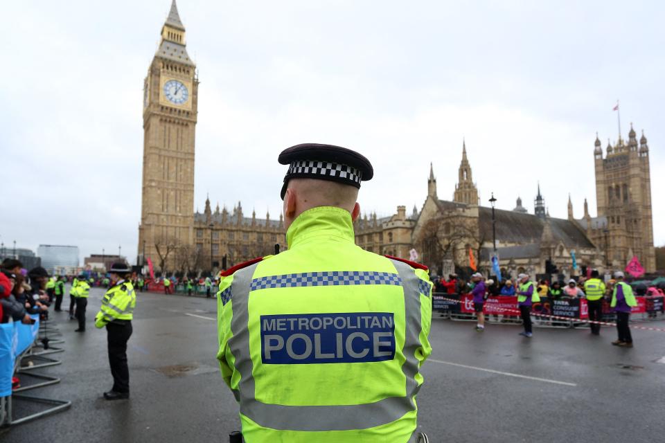 An officer in the Metropolitan Police force stands on duty as competitors run past the Palace of Westminster (AFP via Getty Images)