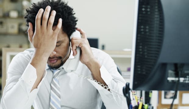 Businessman on phone at desk hand on forehead