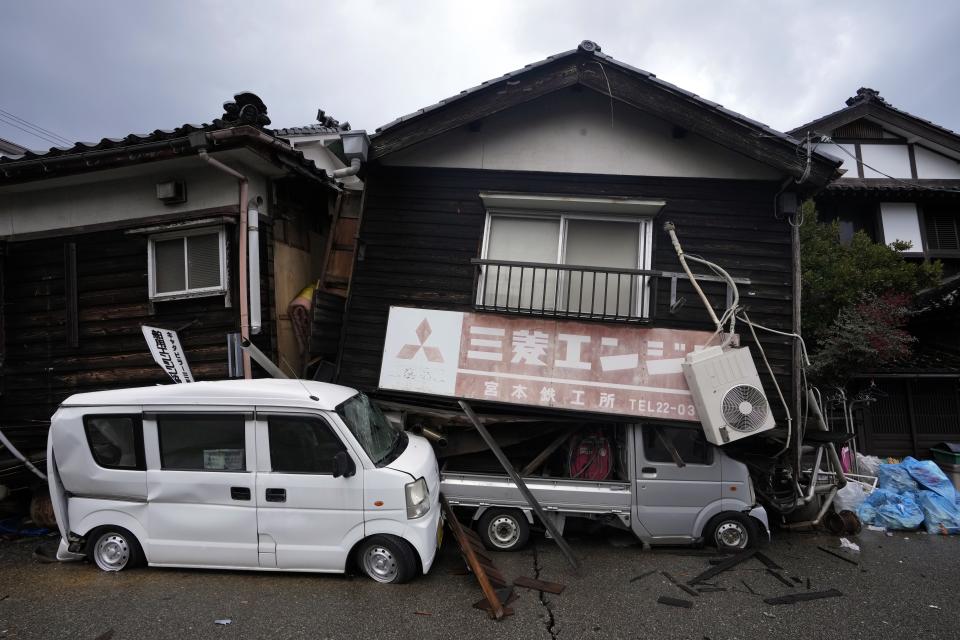Crashed vehicles by collapsed houses are seen in Wajima in the Noto peninsula facing the Sea of Japan, northwest of Tokyo, Sunday, Jan. 7, 2024. Monday's temblor decimated houses, twisted and scarred roads and scattered boats like toys in the waters, and prompted tsunami warnings. (AP Photo/Hiro Komae)