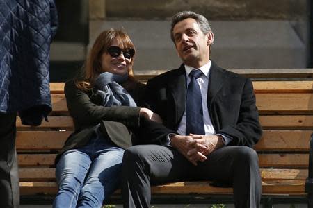 Former French President Nicolas Sarkozy (R) sits on a bench with his wife and singer Carla Bruni-Sarkozy after voting at a polling station in the first round in the French mayoral elections in Paris, March 23, 2014. REUTERS/Benoit Tessier