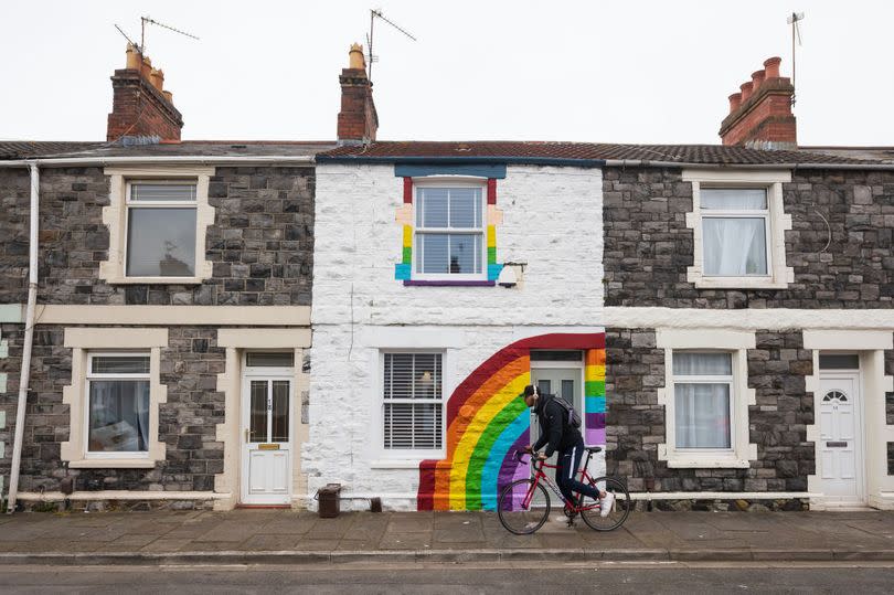 A man rides his bike passed a terraced house painted with a rainbow in support of the NHS in Splott in April 2020