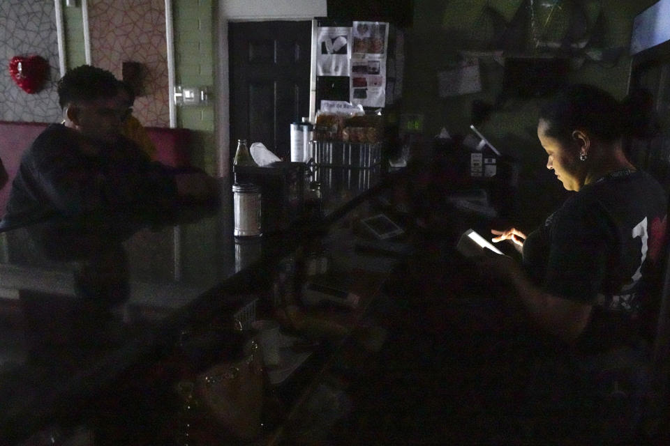 Ada Duarte takes to go orders using only the light of her phone after losing power at Anita's Honduras Restaurant on Sowden Road in the aftermath of a severe storm on Friday, May 17, 2024, in Houston. The widespread destruction brought much of Houston to a standstill as crews raced to restore power and remove uprooted trees and debris. (Brett Coomer/Houston Chronicle via AP)