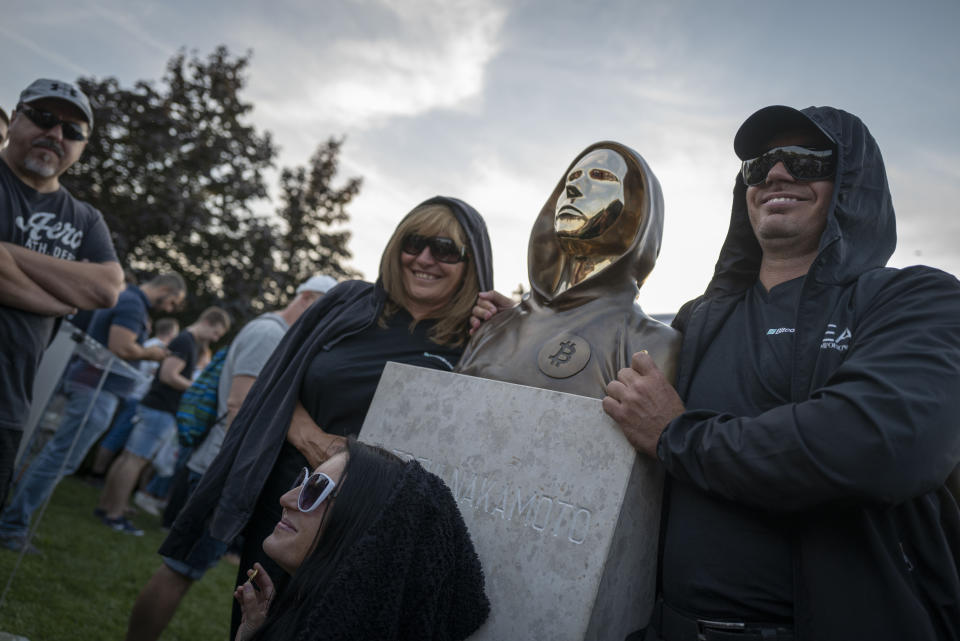 People pose with a newly unveiled statue of the mysterious developer of the Bitcoin digital currency in Budapest, Hungary, Thursday, Sept. 16, 2021. A bronze statue was unveiled in Hungary’s capital on Thursday which its creators say is the first in the world to pay homage to the anonymous creator of the Bitcoin digital currency. Erected in a business park near the Danube River in Budapest, the bust sits atop a stone plinth engraved with the name of Satoshi Nakamoto, the pseudonym of the mysterious developer of Bitcoin whose true identity is unknown. (AP Photo/Bela Szandelszky)