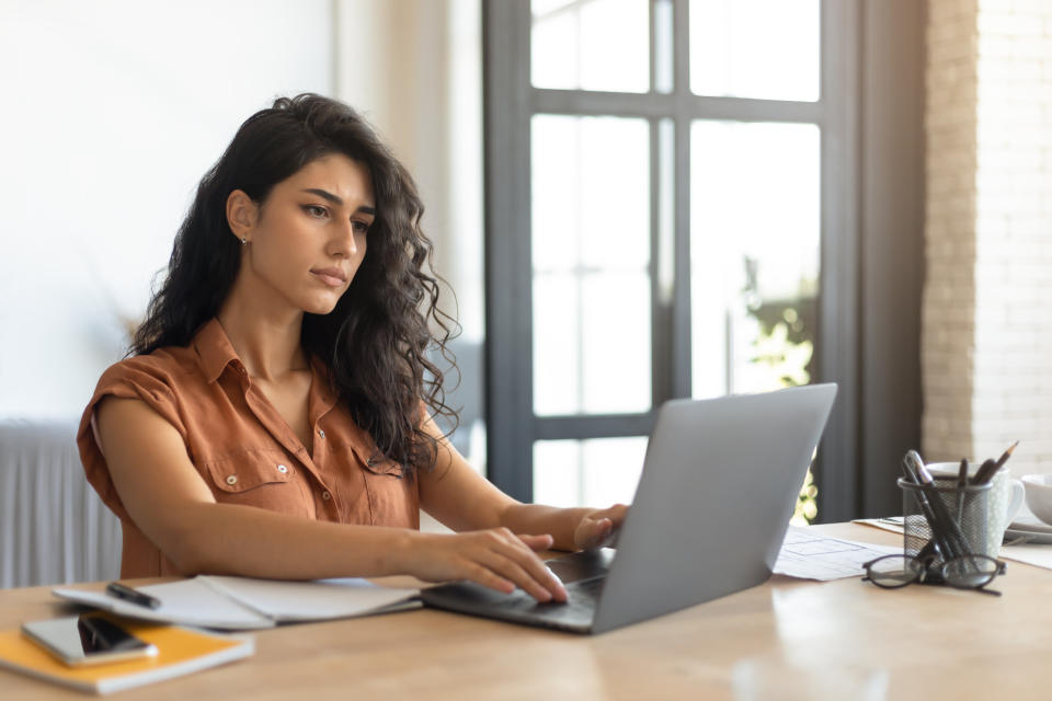 Focused young female freelancer working online, using laptop computer at home