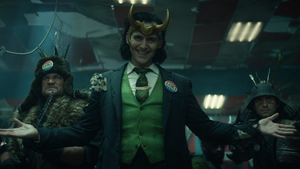 Loki wears his horned helmet and a three-piece suit before his army.