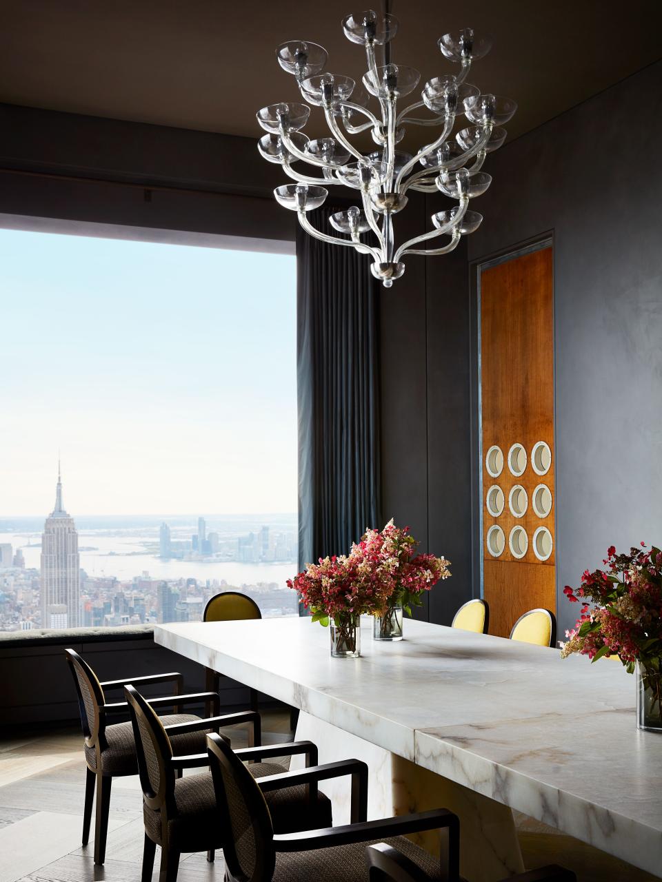 In the dining room, Jean Royère armchairs surround an alabaster table by Rick Owens from Carpenters Workshop gallery. Curtains of Lisio silk taffeta, Seguso chandelier, and door panel with portholes by Jean Prouvé.