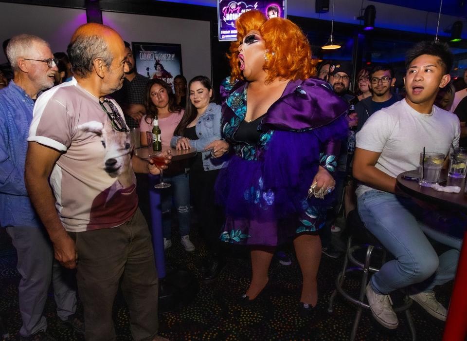 A drag queen surrounded by an audience of men.