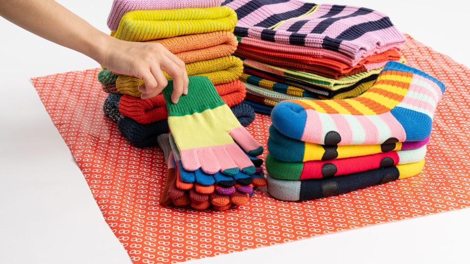 a person putting a colorful knitted hat on a pile of colorful yarn