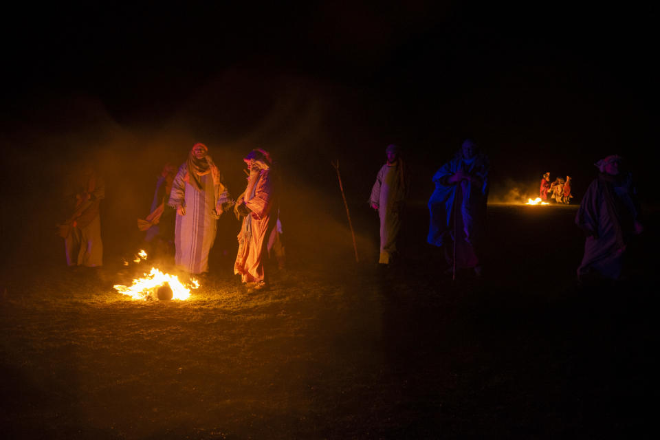 People dressed in shepherd's clothing huddled around fires at night
