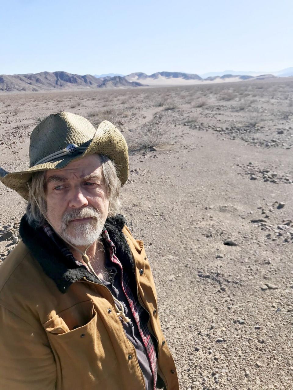 A man in a straw cowboy hat stands in the desert.