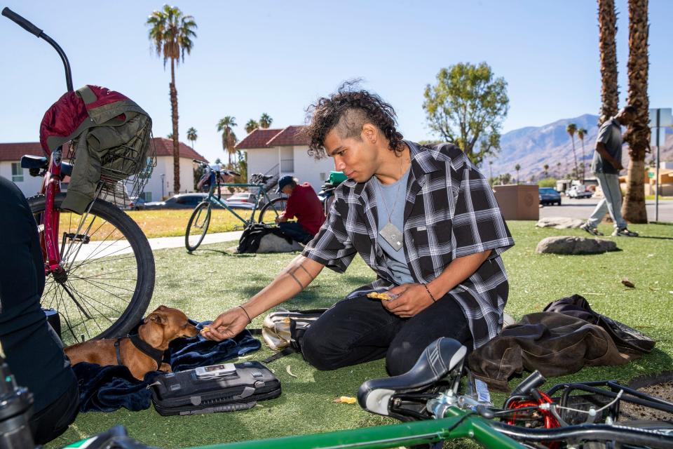 Isaac Hernandez, 27, who is experiencing homelessness offers a friend's dog some food near Baristo Park at the corner of South Calle Encilia and Saturnino Road in Palm Springs, Calif., on October 26, 2021. The City of Palm Springs will temporarily close the park for about six weeks. 
