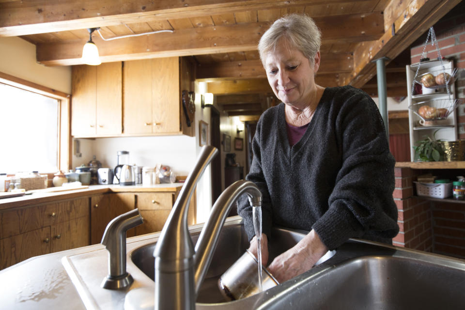 Catherine Maynard, a natural resource analyst for the U.S. Department of Agriculture, washes dishes in her home in Rimini, Mont., on Feb. 18, 2019. “The fact that bottled water is provided is great. ... Where it falls short is it’s not piped into our home. Water that’s piped into our home is still contaminated water. Washing dishes and bathing _ that metal-laden water is still running through our pipes,” she says. (AP Photo/Janie Osborne)
