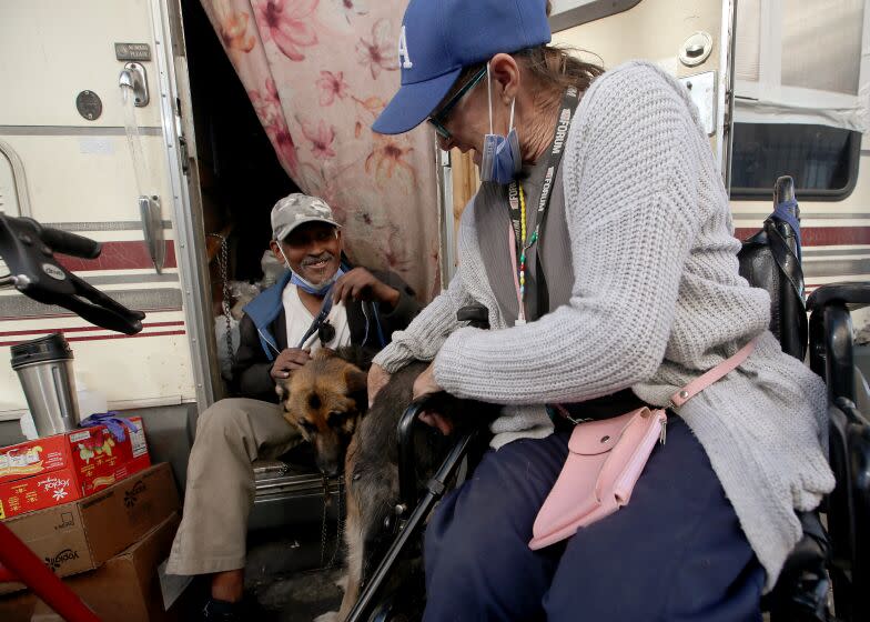 LOS ANGELES , CALIF. - NOV. 22, 2022. Larry Gray, 60, and his partner, Lorna Walker, 57, play with their dog outside a motorhome that currently serves as their home. This time of year they are able to stock up on food and other necessities from holiday grocery and meal giveaways. (Luis Sinco / Los Angeles Times)