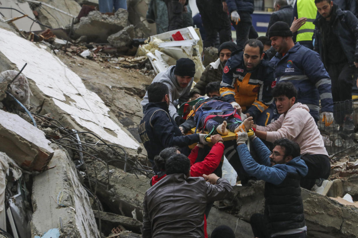 People and emergency teams rescue a person on a stretcher from a collapsed building.