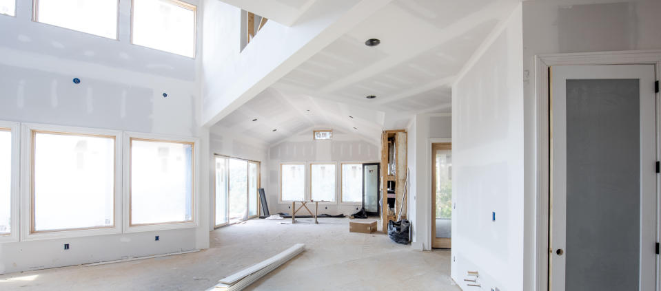 An unfinished open-concept room with large windows, a high ceiling, and unpainted walls, ready for further construction work