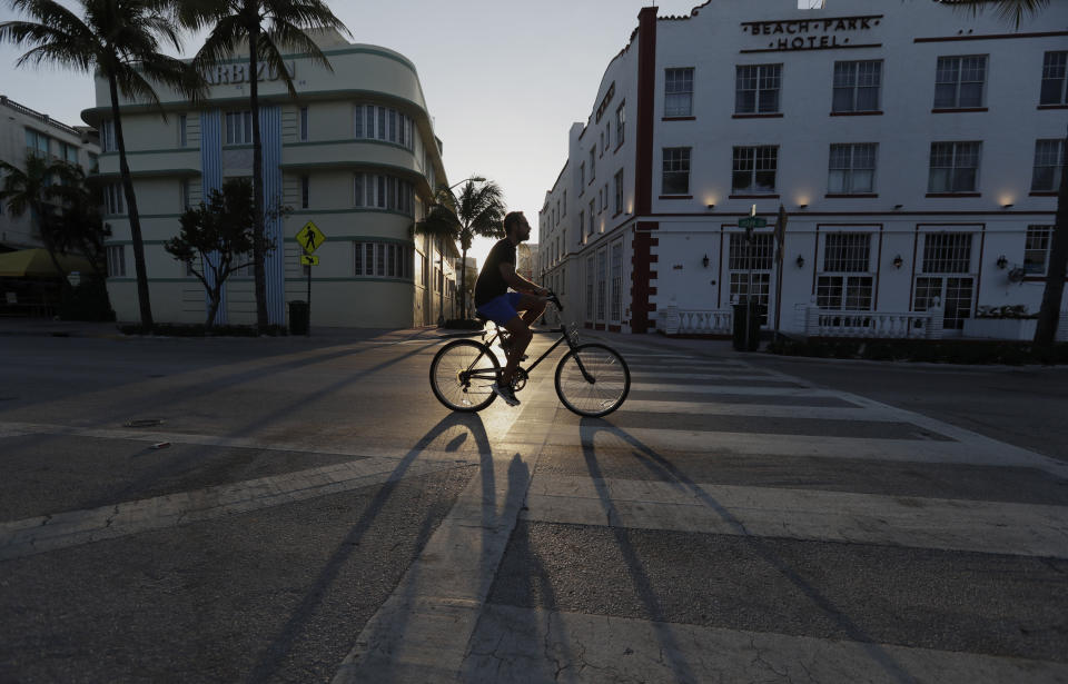 A cyclist rides past Art Deco hotels on normally bustling streets as the sun sets, Wednesday, March 25, 2020, in Miami Beach, Florida's famed South Beach. The new coronavirus causes mild or moderate symptoms for most people, but for some, especially older adults and people with existing health problems, it can cause more severe illness or death.(AP Photo/Wilfredo Lee)