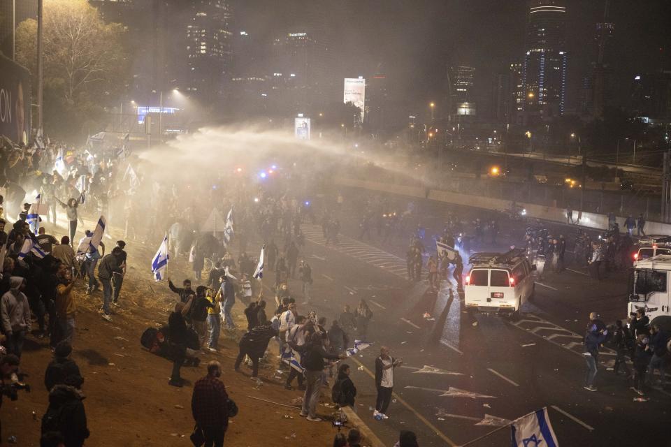 Israeli police use a water cannon to disperse demonstrators blocking a highway during a protest against plans by Prime Minister Benjamin Netanyahu's government to overhaul the judicial system in Tel Aviv, Israel, Monday, March 27, 2023. Tens of thousands of Israelis have poured into the streets across the country in a spontaneous outburst of anger after Prime Minister Benjamin Netanyahu abruptly fired his defense minister for challenging the Israeli leader's judicial overhaul plan. (AP Photo/Oren Ziv)