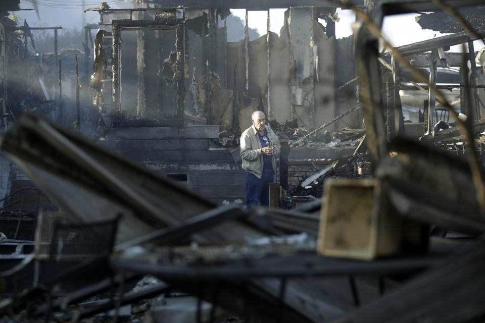 FILE - Dick Marsala looks through debris from his destroyed home after a wildfire roared through the Rancho Monserate Country Club, Dec. 8, 2017, in Bonsall, Calif. Environmental groups have been arguing in California courts that developers are not fully considering the risks of wildfire and choked evacuation routes when they plan housing developments near fire-prone areas. (AP Photo/Gregory Bull, File)