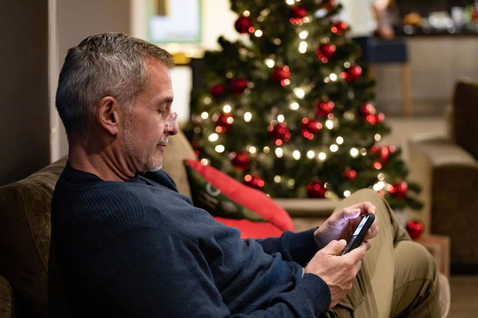 Mature man at home texting on his cell phone on Christmas Eve and using reading glasses - holiday season concepts
