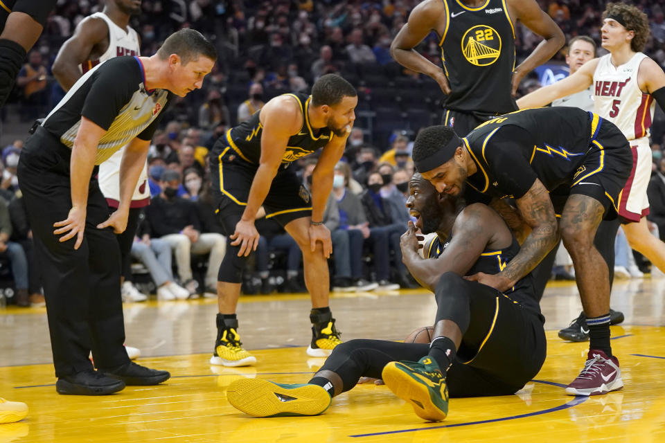 Golden State Warriors forward Draymond Green, bottom, is helped up by guard Gary Payton II while talking to referee Nick Buchert, left, during the first half of an NBA basketball game against the Miami Heat in San Francisco, Monday, Jan. 3, 2022. (AP Photo/Jeff Chiu)