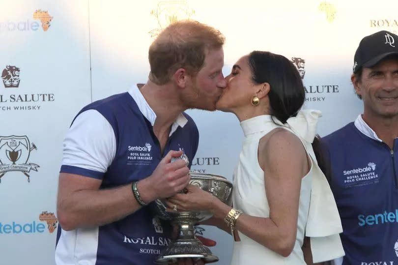 The Duchess of Sussex presents the trophy to her husband, the Duke of Sussex with a kiss after his team the Royal Salute Sentebale Team defeated the Grand Champions Team