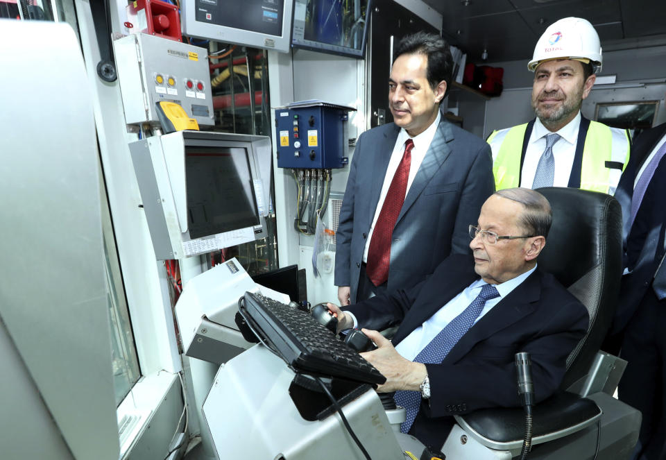 In this photo released by Lebanon's official government photographer Dalati Nohra, Lebanese Prime Minister, left, stands next to Lebanese President Michel Aoun, seated, inside a control room of the drilling ship Tungsten Explorer which will be conducting drilling operations of the first exploration well, located approximately 30 kilometers (18 miles) offshore from the capital Beirut Lebanon, Thursday, Feb. 27, 2020. Aoun inaugurated the Mediterranean country's first offshore exploratory drilling for oil and gas, calling it a "historic day" for the cash-strapped country. (Dalati Nohra via AP)