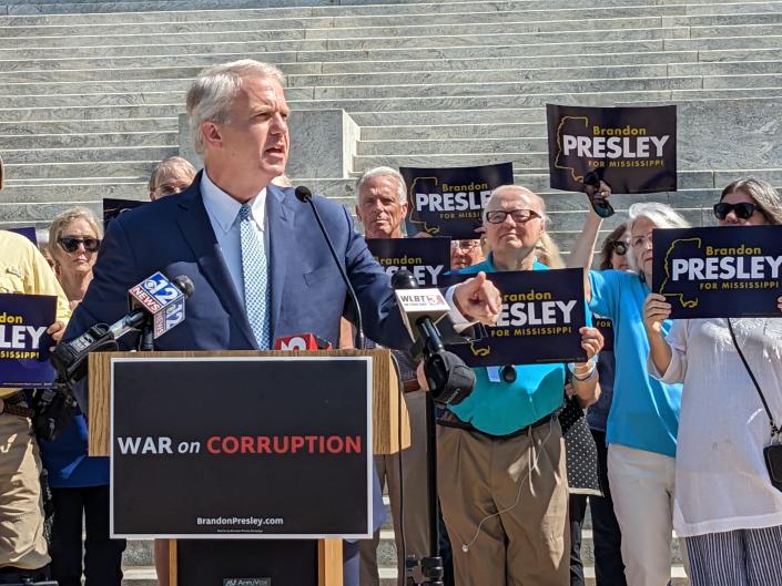 Brandon Presley at the microphone with a crowd supporters behind him holding placards with his name and a poster on the podium saying : War on Corruption.