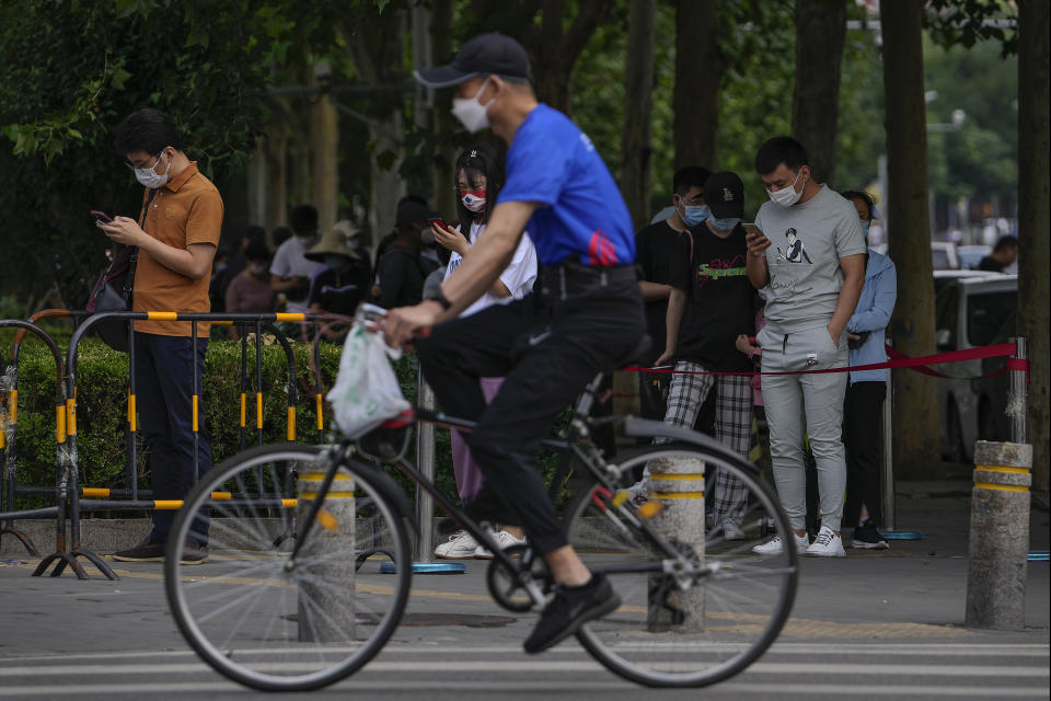 A bicyclist passes residents lining up for coronavirus testing in Beijing, Tuesday, June 14, 2022. (AP Photo/Andy Wong)