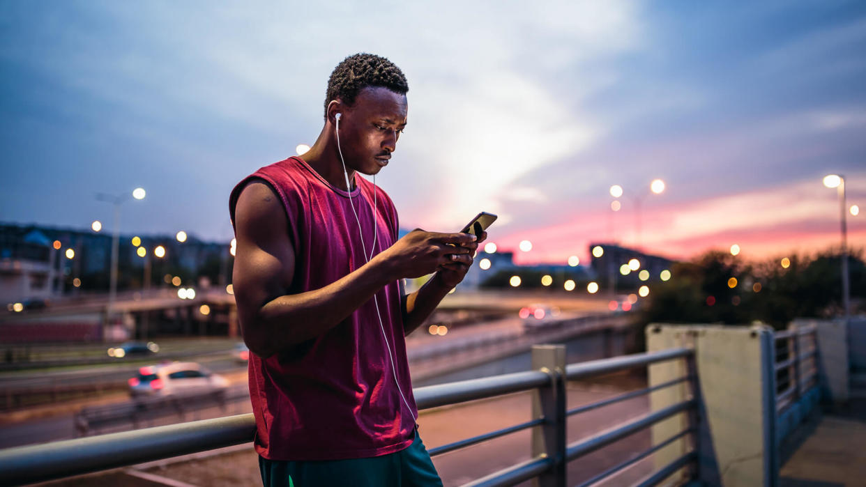 Young African men resting after training outdoors, in urban city environment, using mobile phone.