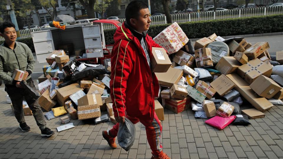 Zusteller sortieren Pakete, die sich an einem Abholpunkt in der Nähe eines Wohnhauses in Peking stapeln. (Bild: dpa)