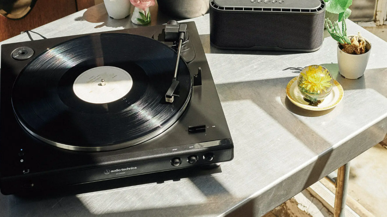  Audio Technica AT-LP60XBT on a table with a bluetooth speaker and two small potted plants in the sun. 