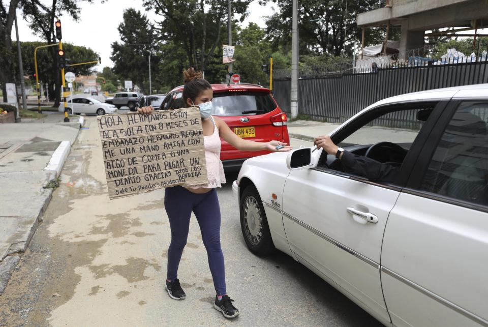 Venezuelan migrant Veronica Hernandez, 20, eight months pregnant, holding a sign with a handwritten message asking for food or money, puts out her hand to receive alms from a driver, in Bogota, Colombia, Tuesday, Feb. 9, 2021. Colombia said Monday it will register hundreds of thousands of Venezuelan migrants and refugees currently in the country without papers, in a bid to provide them with legal residence permits and facilitate their access to health care and legal employment opportunities. (AP Photo/Fernando Vergara)